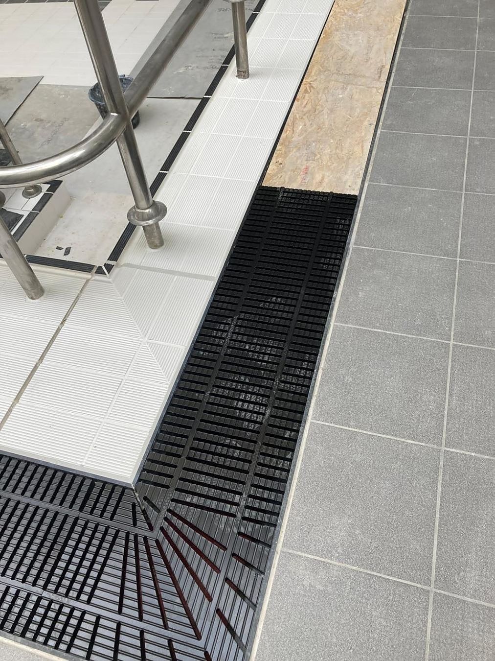 New black grating and tile junction at the pool corner.